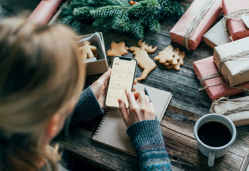 Woman planning holding a phone with a calendar on the screen working on christmas desk