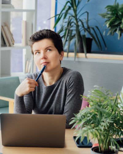 Middle aged minded pensive employee business woman in casual clothes holds a pen, works at office