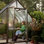 Woman works remotely on laptop in glasshouse at backyard
