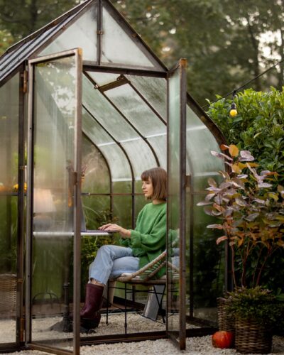 Woman works remotely on laptop in glasshouse at backyard