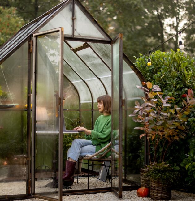 Woman works remotely on laptop in glasshouse at backyard